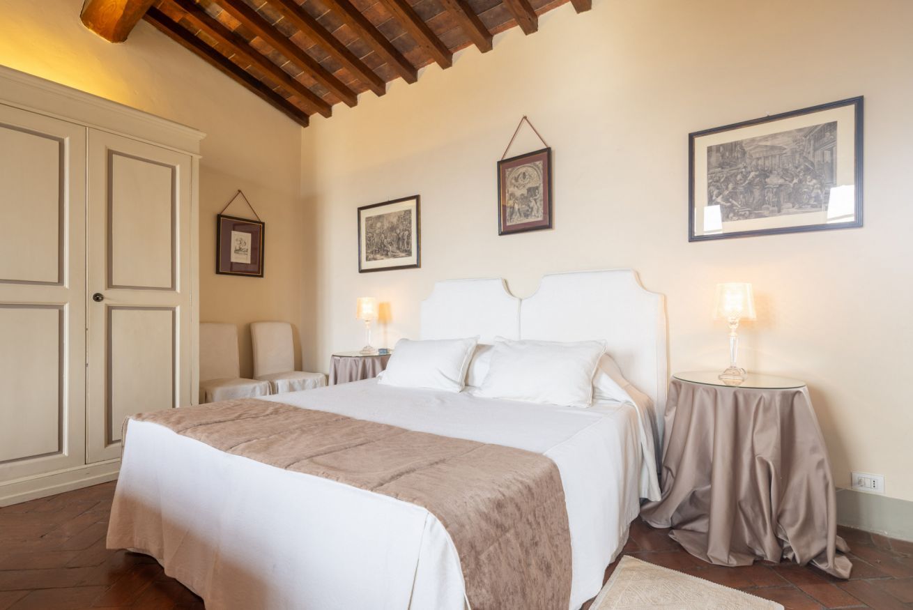 Um quarto com uma cama grande, duas mesas de cabeceira com abajures, teto de madeira e quadros nas paredes.