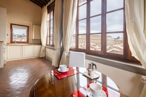 A dining area with a table set for two, a window with curtains, and a view of a cityscape.