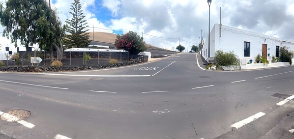 A road with a white building on the right, a signpost, and a tree with red flowers. - Villa Medinilla With Private Pool in Conil (Tías)