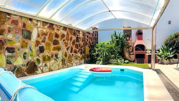Ein Schwimmbecken mit Glasdach, umgeben von einer Steinmauer und verschiedenen Pflanzen.