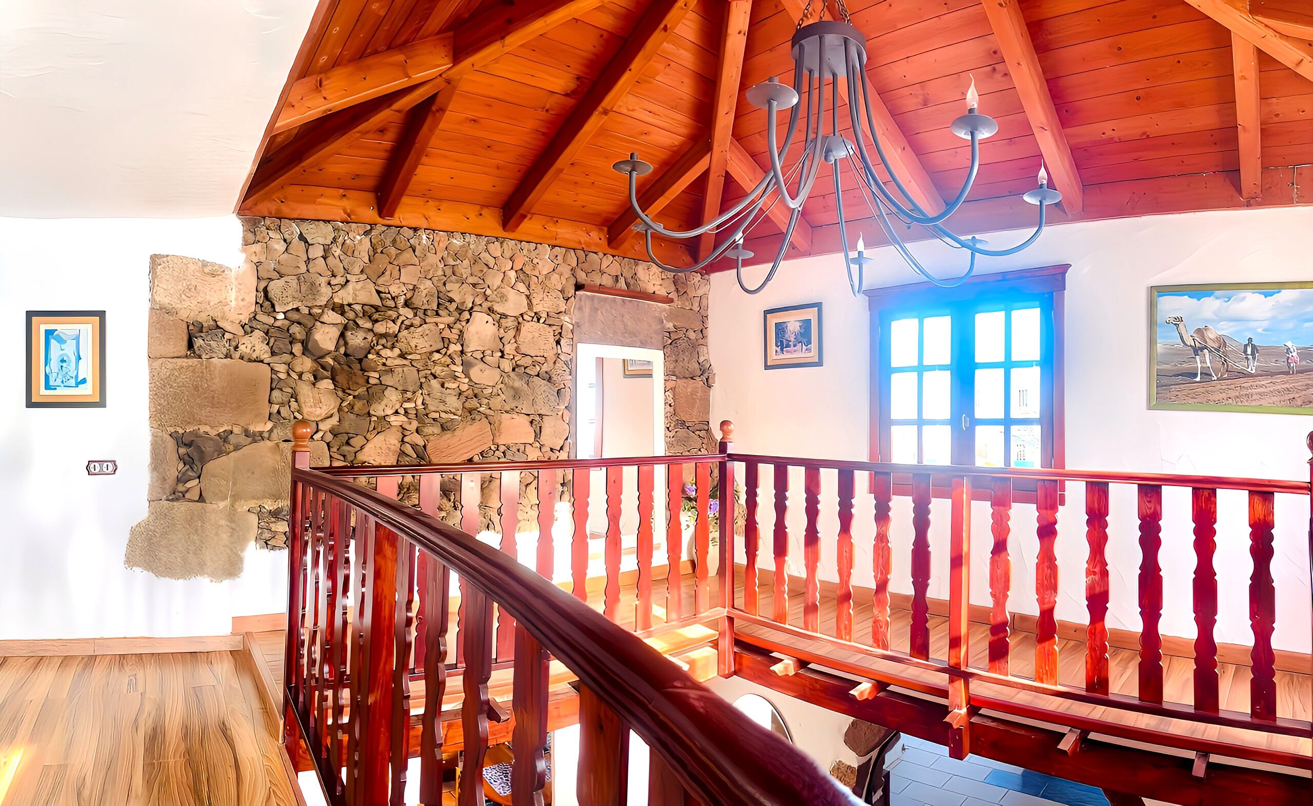 A spacious room with a wooden ceiling, stone wall, and a wooden staircase with a red railing.