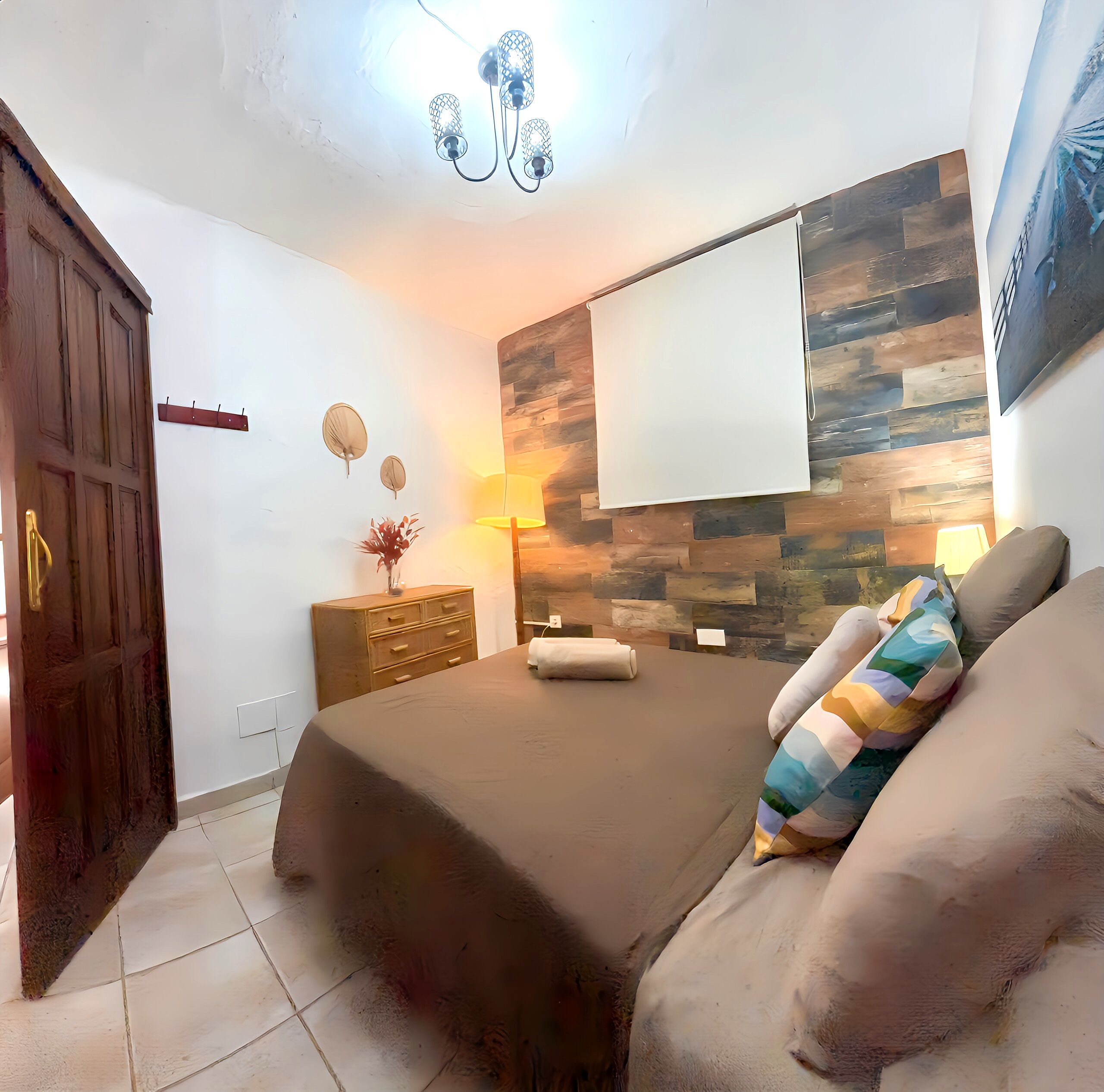 A bedroom with a bed, a wooden wardrobe, a nightstand with a lamp, and a wall-mounted TV.