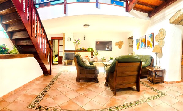 A spacious living area with a wooden staircase, a television, and a dining table with chairs.