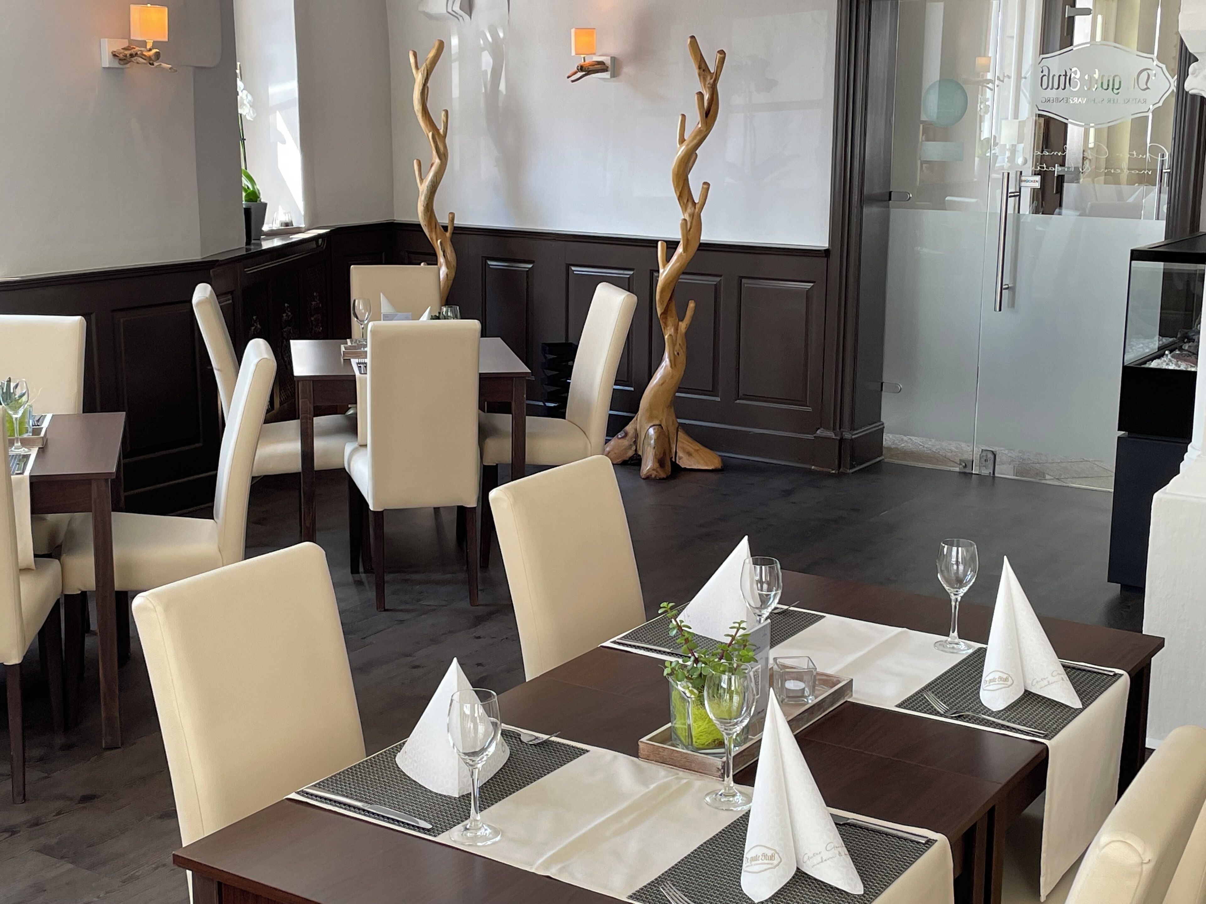 A restaurant interior with high-backed chairs, dark wood tables, and decorative wooden branches.