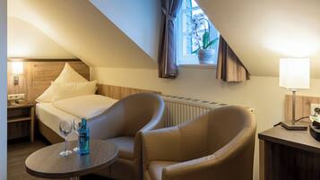 A cozy hotel room with a bed, two armchairs, a small table with drinks, a window with curtains, and a radiator.
