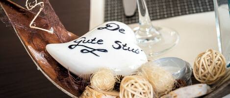 A decorative bowl with a white ceramic piece inscribed with "De Gute Stube" surrounded by natural elements like twine and pine cones.