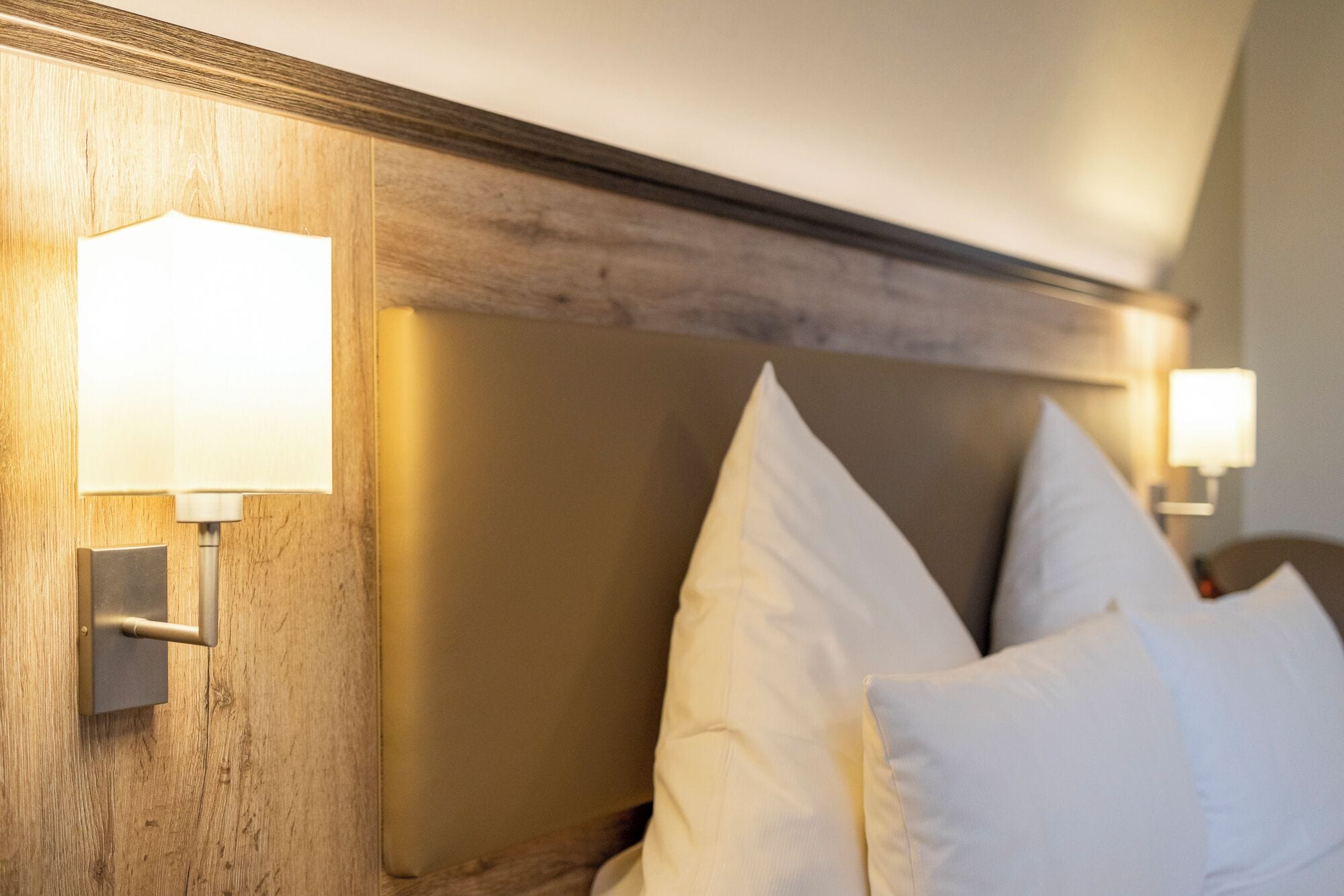 Une chambre d’hôtel avec une tête de lit en bois, deux lampes de chevet et des oreillers blancs.