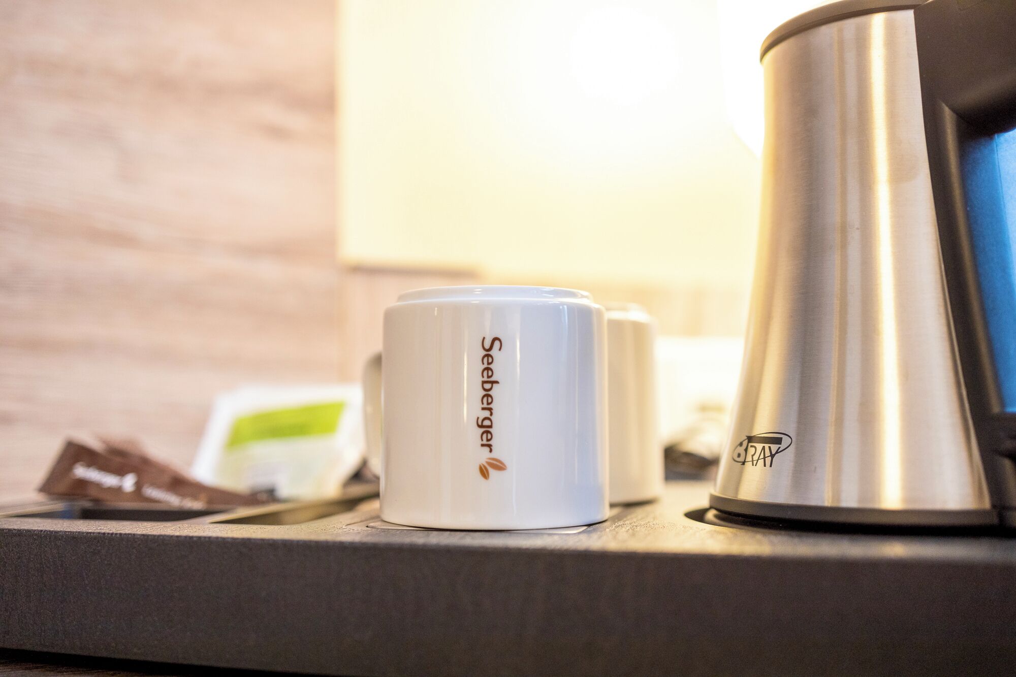 A coffee maker and two white mugs with the Seeburger logo on a countertop.