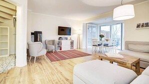 Un salon moderne avec un canapé, une table basse et un téléviseur. On y trouve également une bibliothèque et un coin repas avec des chaises.