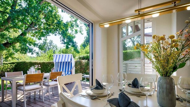 Un espace de restauration en plein air avec une table dressée pour quatre personnes, des chaises et une chaise longue à rayures.