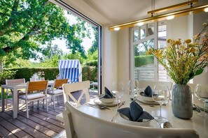 Un espace de restauration en plein air avec une table dressée pour quatre personnes, des chaises et une chaise longue à rayures.