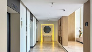 Corredor moderno de hotel com piso de mármore, um espelho redondo e um banco.