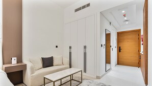 Quarto de hotel moderno com sofá, uma pequena mesa, um guarda-roupa e uma porta de madeira.