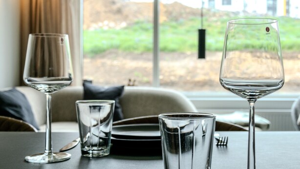 A dining table with two wine glasses and a water glass, set against a window with a view of buildings and greenery.