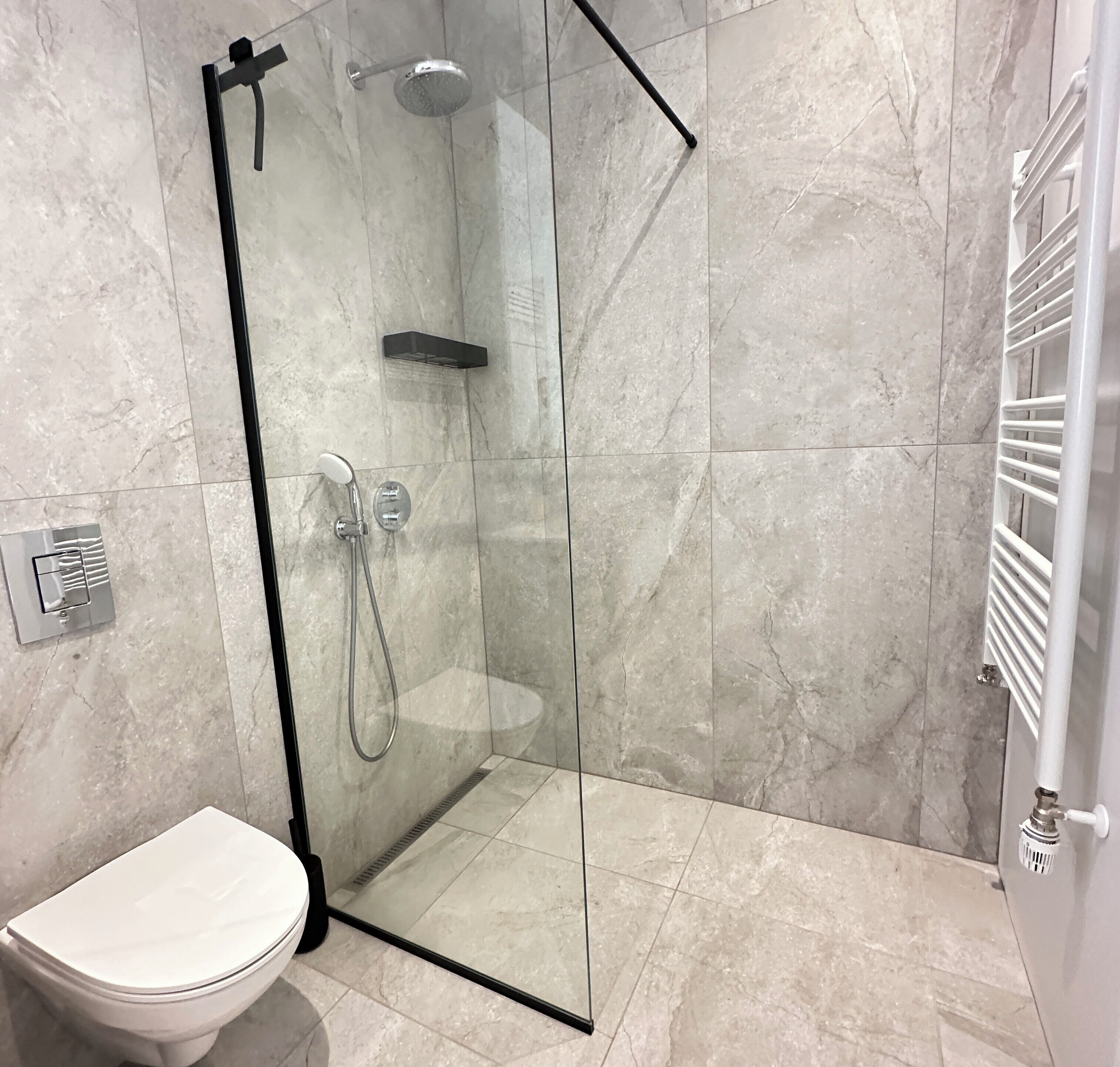 A modern bathroom with a glass-enclosed shower, a toilet, and a built-in heater.