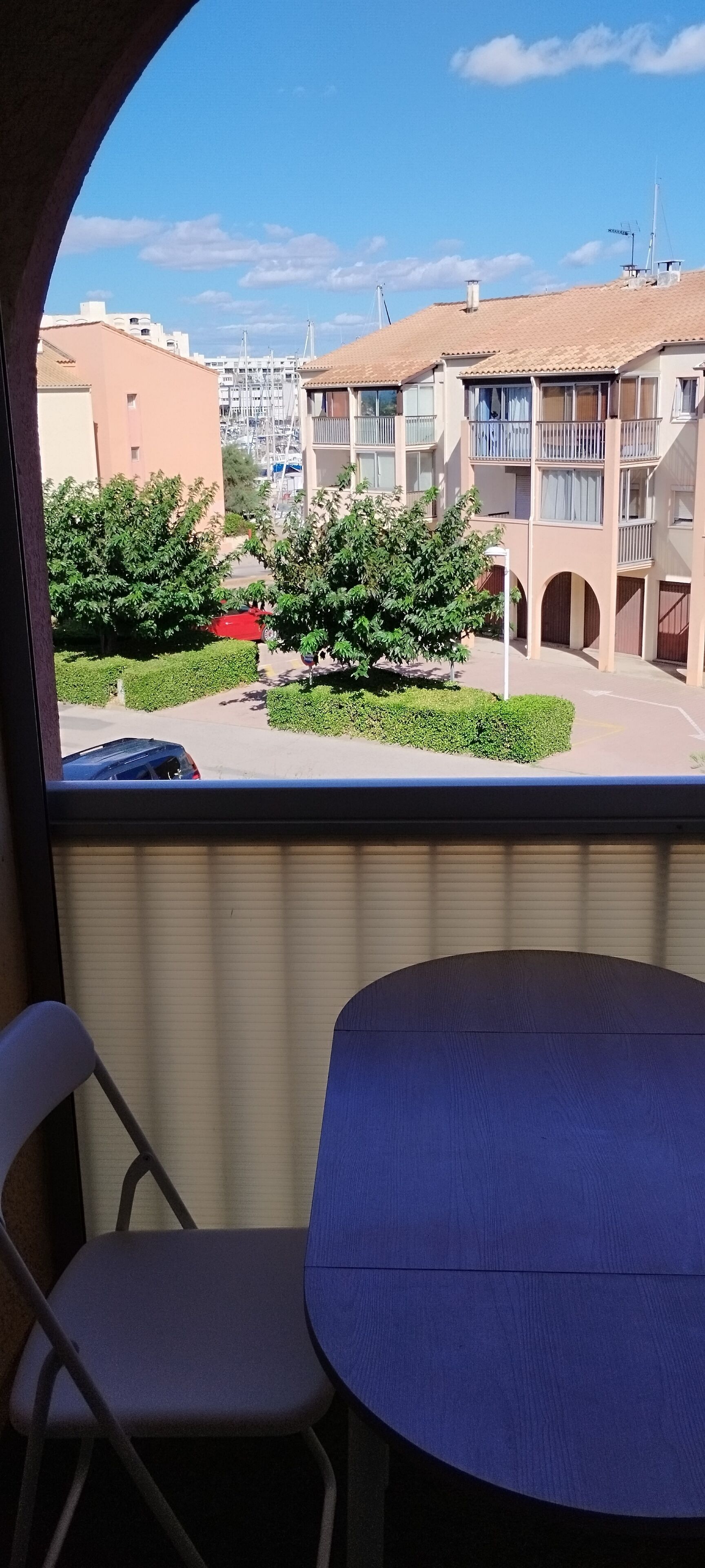 A balcony with a table and chairs, overlooking a residential area with buildings and greenery.