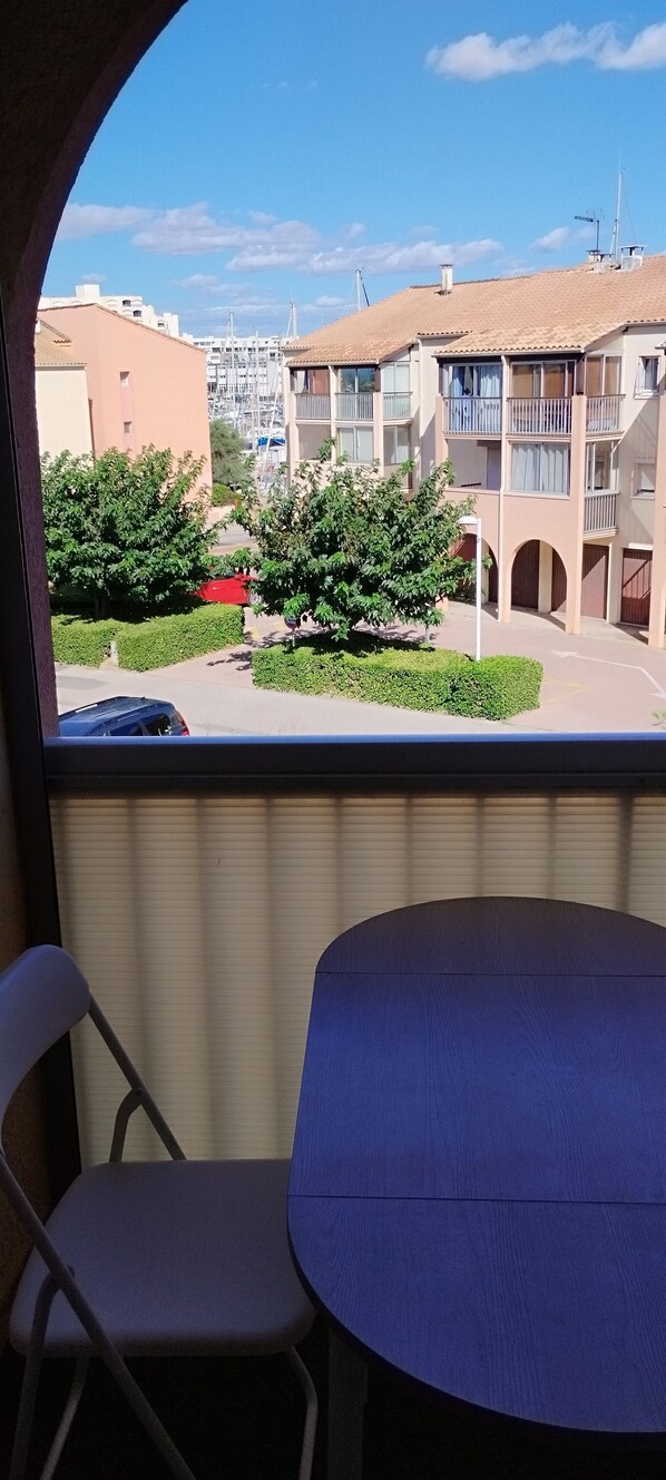A balcony with a table and chairs, overlooking a residential area with buildings and greenery.