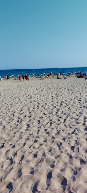 A sandy beach with footprints and people in the distance.