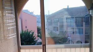 A room with a sliding glass door leading to a balcony with two white chairs and a table.