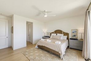 Un dormitorio con cama, mesitas de noche, ventilador de techo y una puerta.