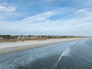 A coastal view with a beach, ocean waves, and a distant shoreline with houses. - 779 Marlin Drive (Fripp Island)