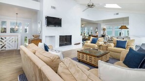 A spacious living room with a fireplace, ceiling fan, and large windows. - 715 Winter Trout Road (Fripp Island)