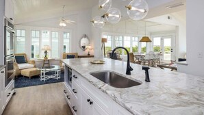 A spacious kitchen with a large island, white cabinetry, and a modern pendant light fixture. - 715 Winter Trout Road (Fripp Island)