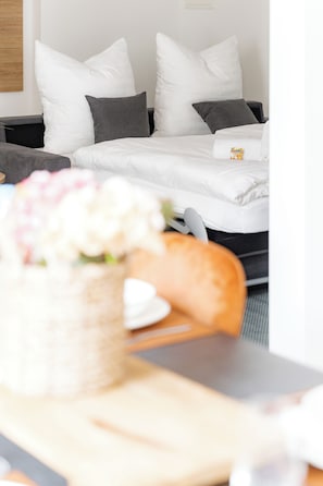 Ein Hotelzimmer mit einem Bett, Kissen, einem Nachttisch mit einer Blumenkorb und einem kleinen Tisch mit Teller und Tasse.