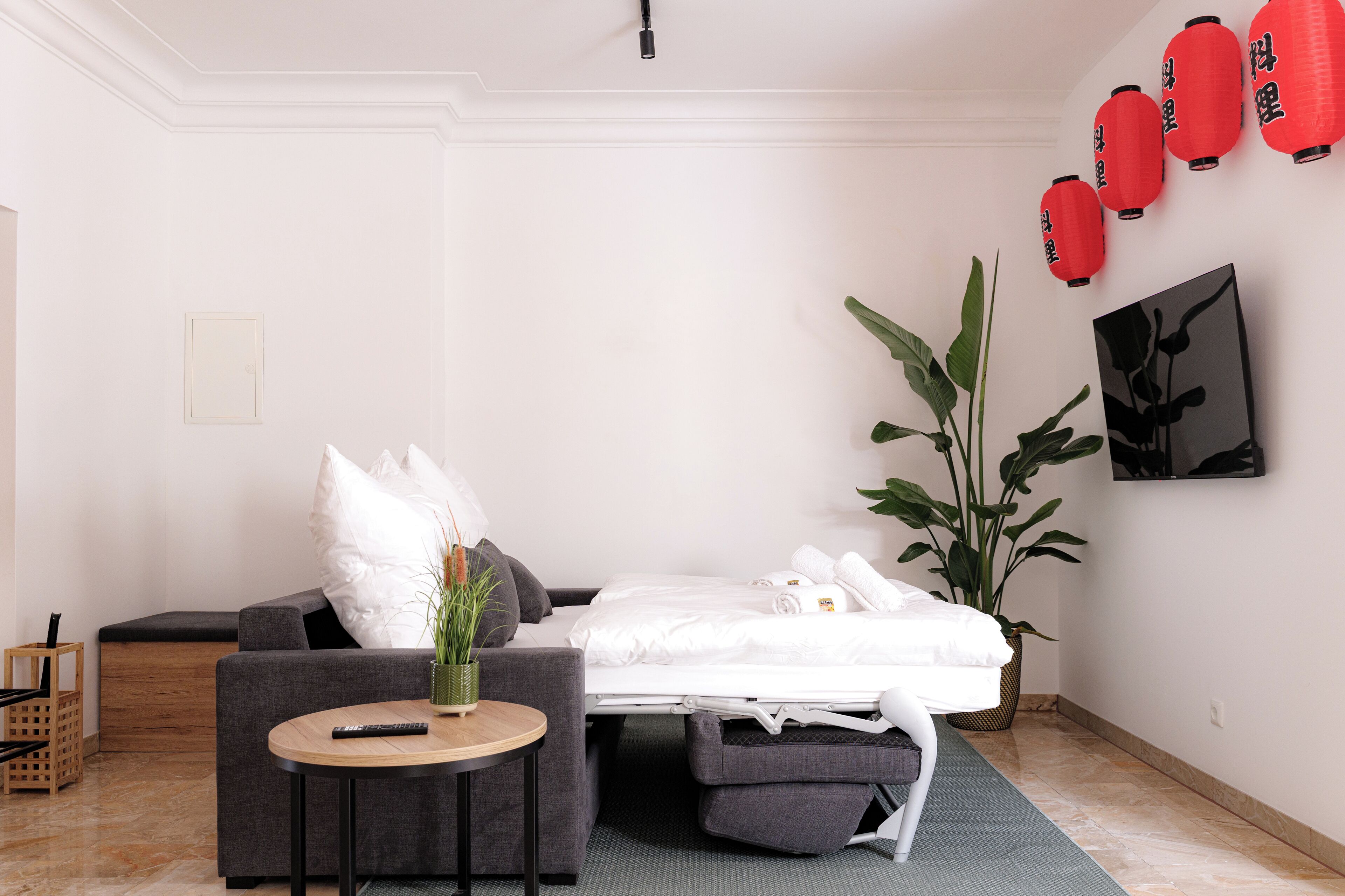 Une chambre d’hôtel minimaliste comprenant un lit, une petite table ronde, un canapé et une grande plante en pot.