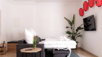 Une chambre d’hôtel minimaliste comprenant un lit, une petite table ronde, un canapé et une grande plante en pot.