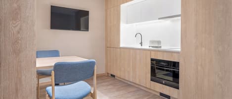 A modern kitchen with wooden cabinets, a built-in oven, a sink, and a dining area with a table and chairs.