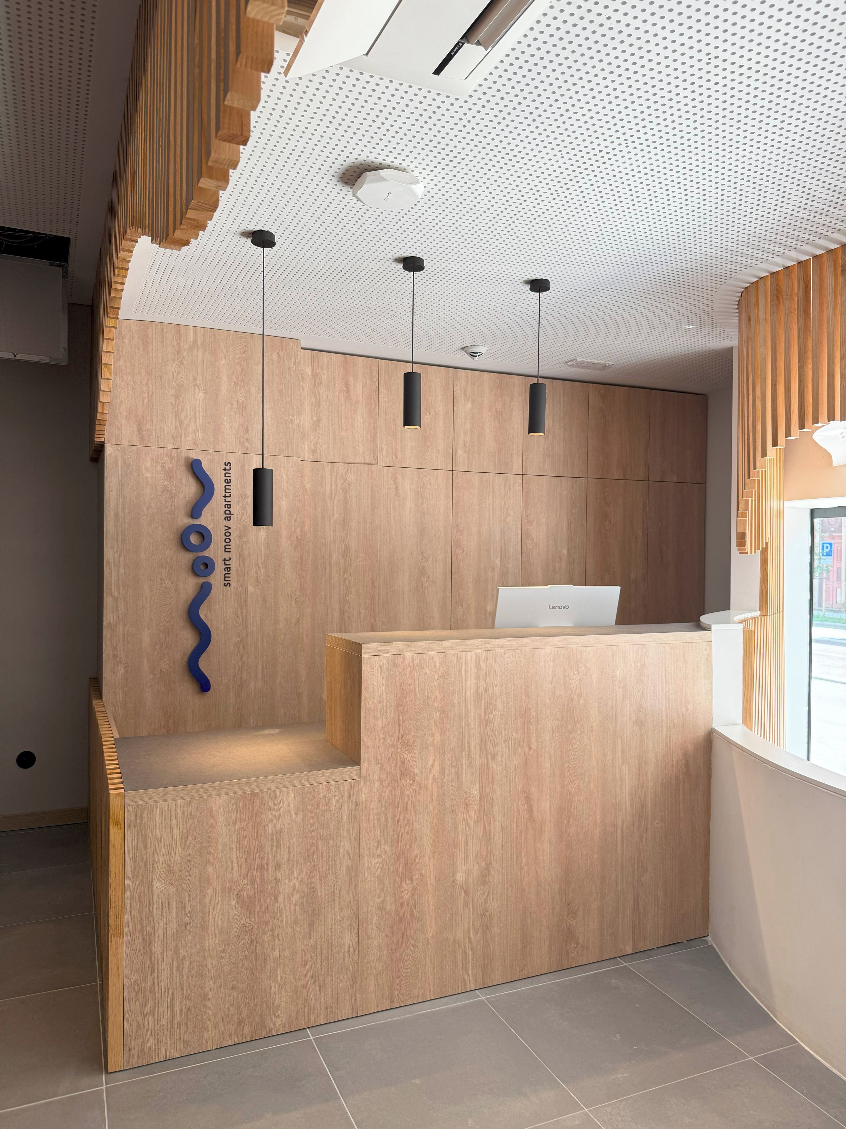 A reception desk with a modern design, featuring a wooden finish and a logo on the wall.