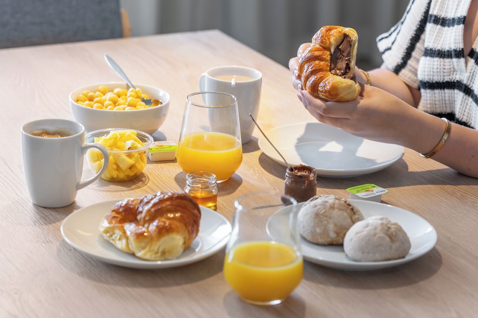 En morgenmadsopsætning med croissanter, frugt, juice og kaffe på et træbord.