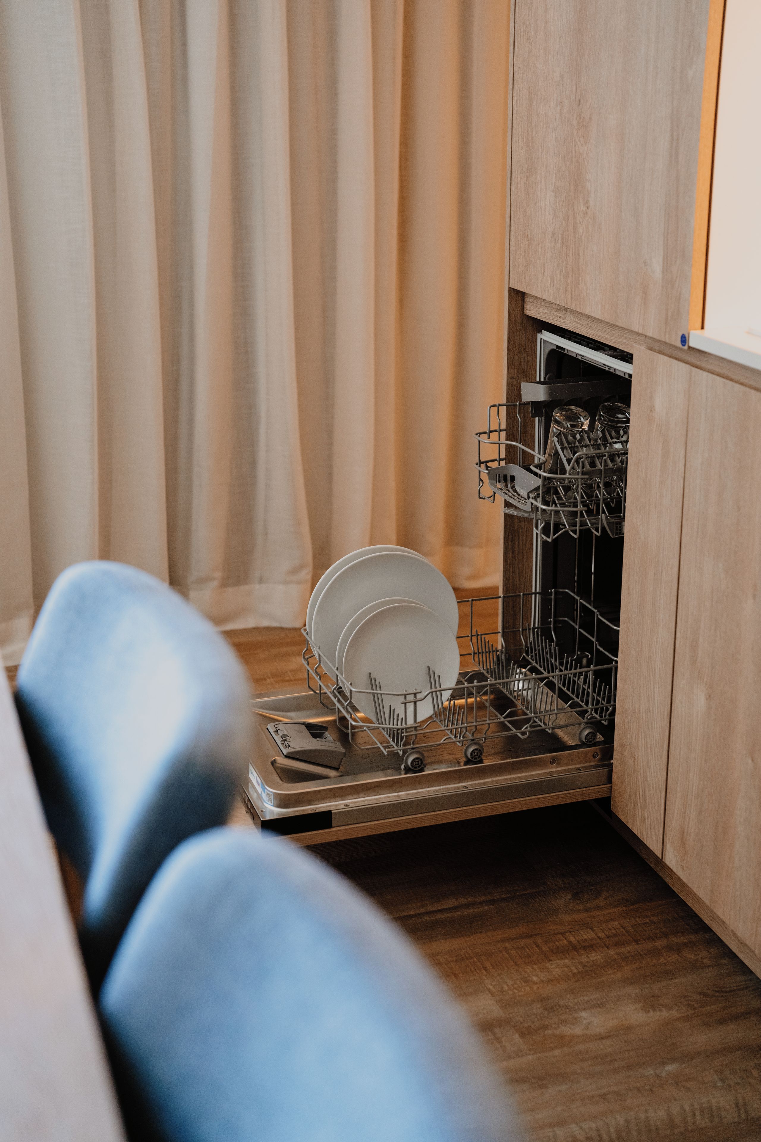 A compact kitchen with a dishwasher, wooden cabinets, and a dining area with a table and chairs.