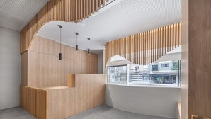 A modern interior with a wooden reception desk, pendant lighting, and a view of the street through large windows. - Moov Apartments Boavista (Porto)