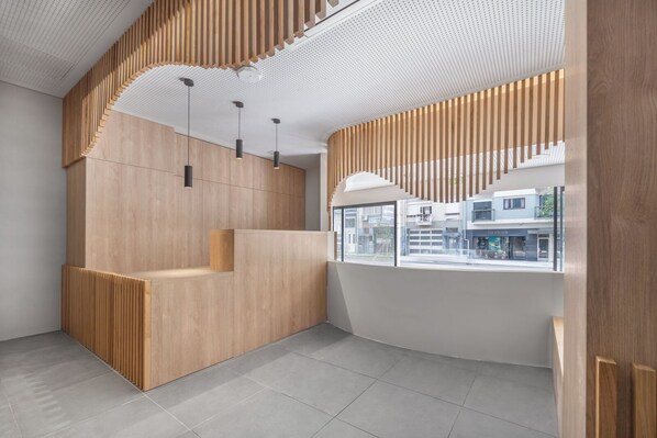Un interior moderno con un mostrador de recepción de madera, iluminación colgante y vistas a la calle a través de amplias ventanas.