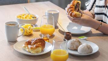 A breakfast setting with croissants, fruit, juice, and coffee on a wooden table.