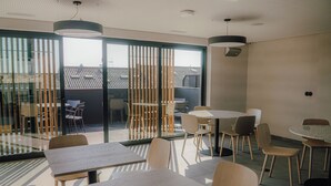 A modern dining area with wooden tables and chairs, large windows, and a view of the outside. - Moov Apartments Boavista (Porto)