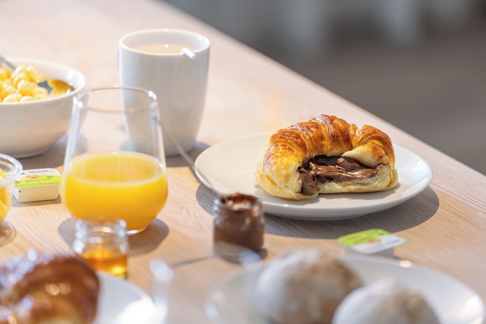 Une table dressée pour le petit-déjeuner avec un sandwich au croissant, un jus d’orange et une tasse de café.