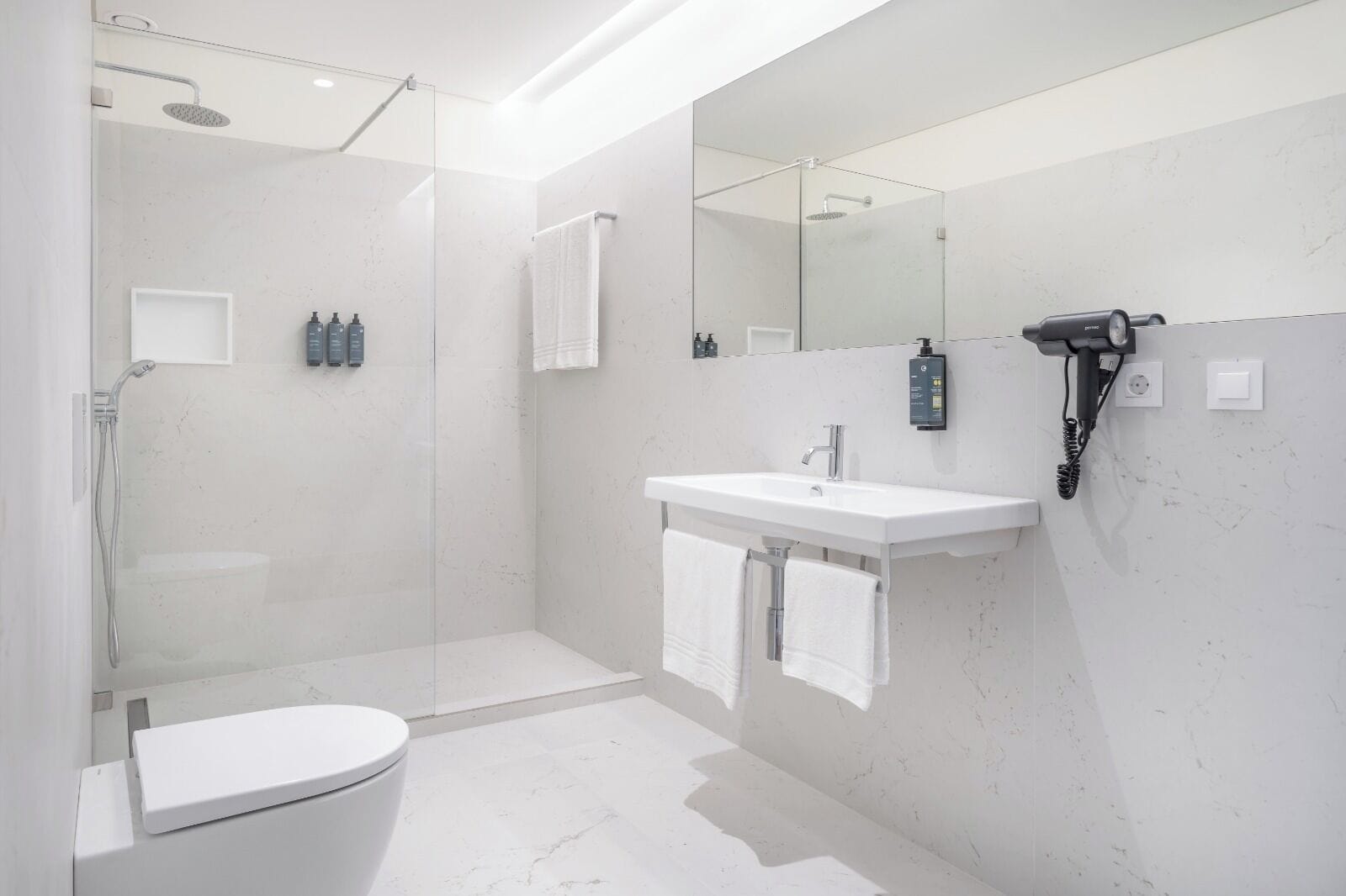 Une salle de bain moderne avec une douche à parois de verre, un lavabo blanc et un sèche-cheveux fixé au mur.