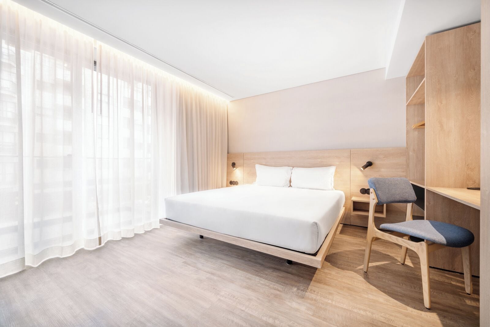 Quarto de hotel moderno com uma cama grande, uma escrivaninha com cadeira e um guarda-roupa.