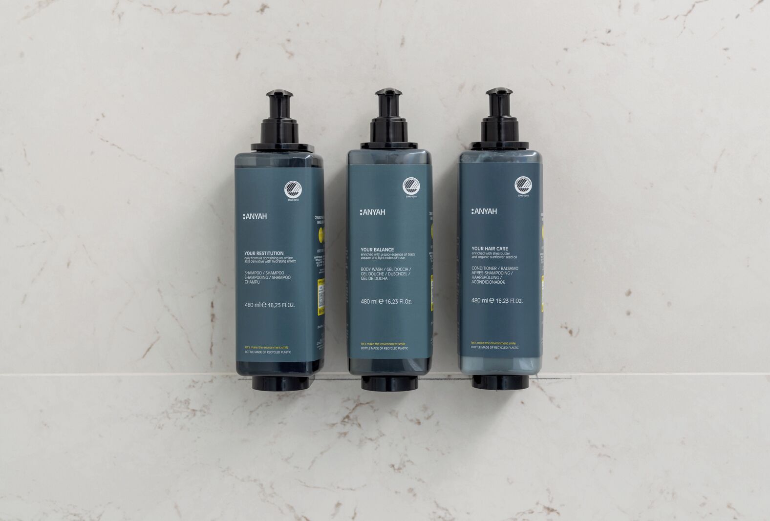Three bottles of Anyah hair care products on a marble surface.