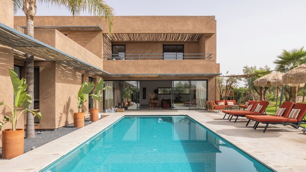 Un bâtiment moderne à deux étages, doté d’une piscine, d’un espace extérieur aménagé et de plantes en pot.