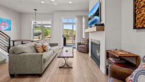 Una sala de estar moderna con sofá, mesa de centro, televisor, chimenea y vistas al exterior.