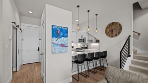 Una cocina moderna con una isla central, taburetes de bar, iluminación colgante y un reloj rústico en la pared.