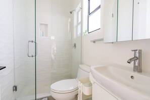 A modern bathroom with a glass-enclosed shower, a white toilet, and a sink with a mirror above it. - Stylish two-bedroom home in Buena Vista with private spa (Miami)
