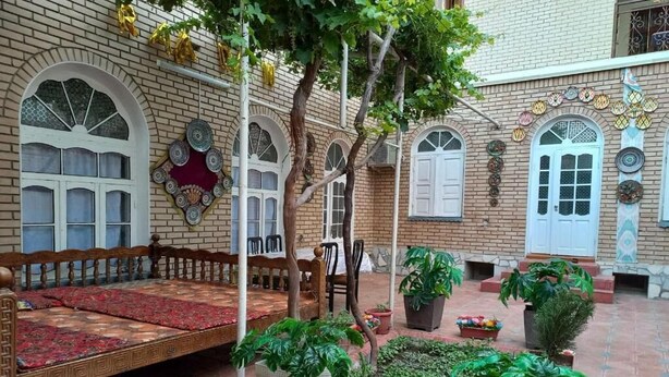 Un patio con un banco de madera, plantas en macetas y suelo de baldosas.