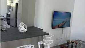 A modern kitchen with a dark countertop, white bar stools, and a painting of a sunset over a pier. - NEW: THE IVORY 3-BEDROOM VILLA (Gros Morne)