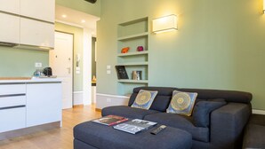 Ein modernes Wohnzimmer mit einem grauen Sofa, einem Couchtisch mit Zeitschriften und einer Küchenzeile mit weißen Schränken und einer Holz Arbeitsplatte.