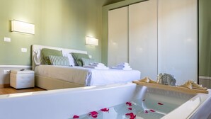Ein modernes Schlafzimmer mit einem großen Bett, einem Nachttisch, einer eingebauten Badewanne mit Rosenblüten und einem Kleiderschrank.